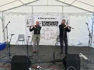 Two men play the flute in a marquee